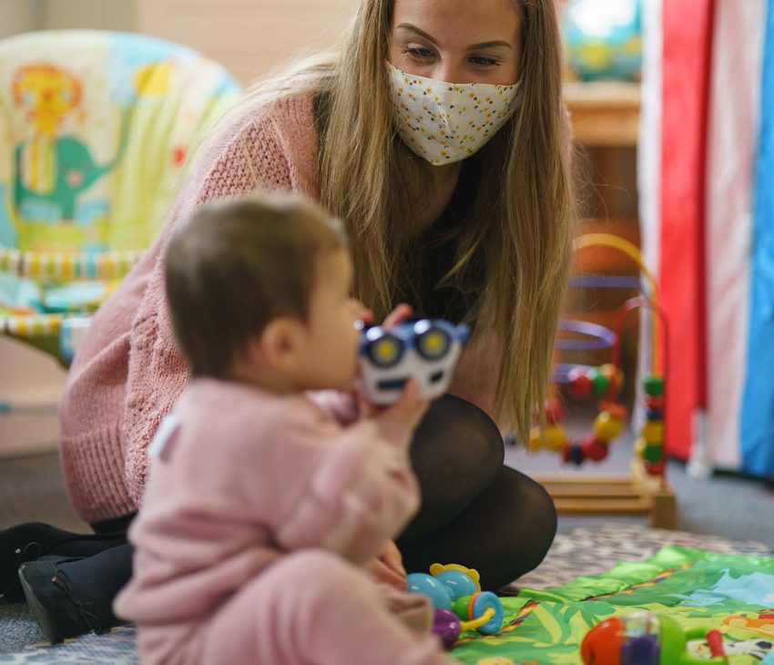 woman in face mask playing with baby