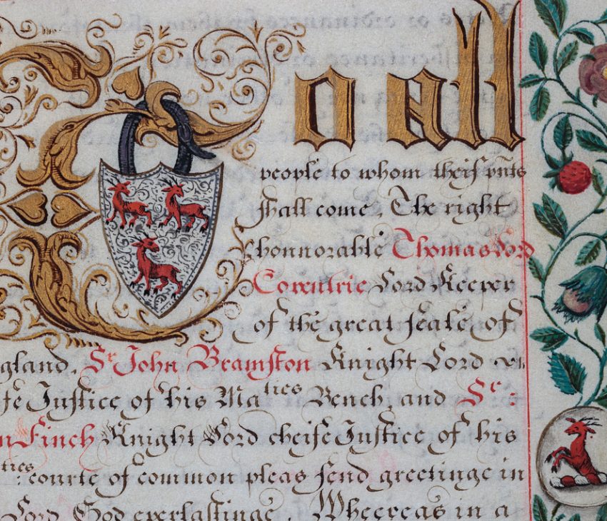 A decorative medieval document with a floral border and a heart shaped shield with three roebucks hanging from a letter