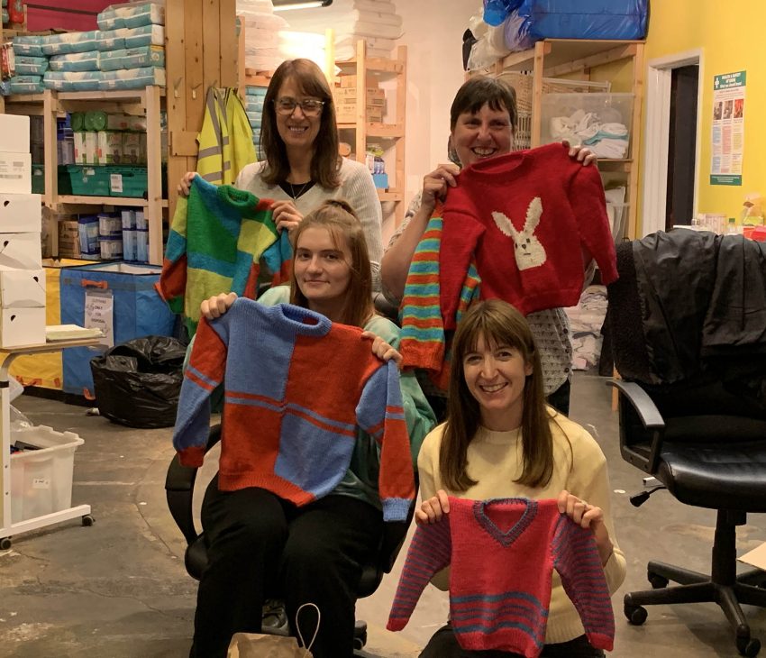 four women holding jumpers in a store room