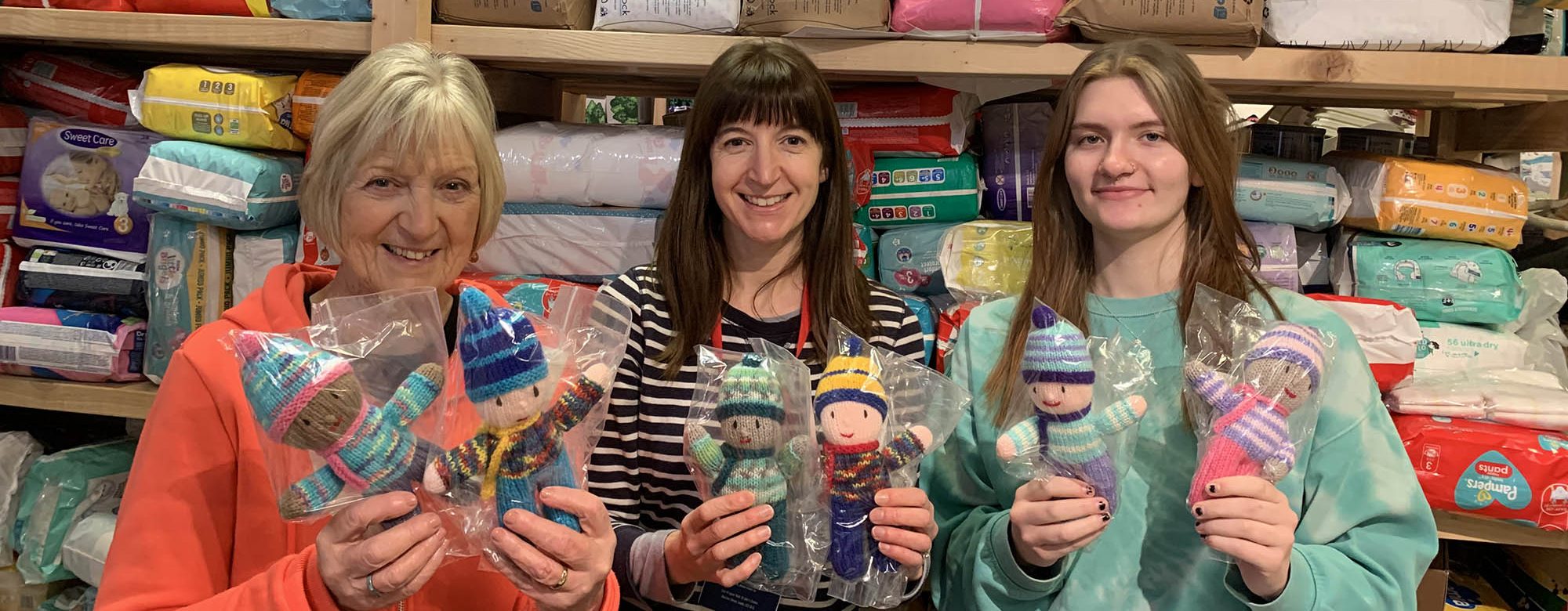 three women holding knitted dolls
