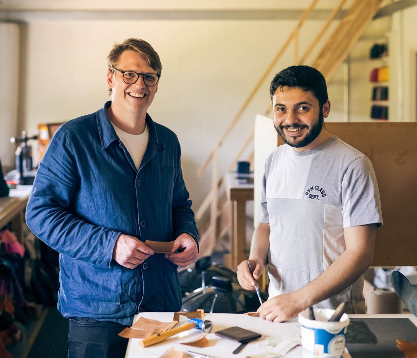 two men in a workshop holding pieces of leather