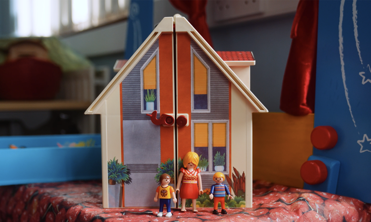 A doll house with a family of figurines standing outside
