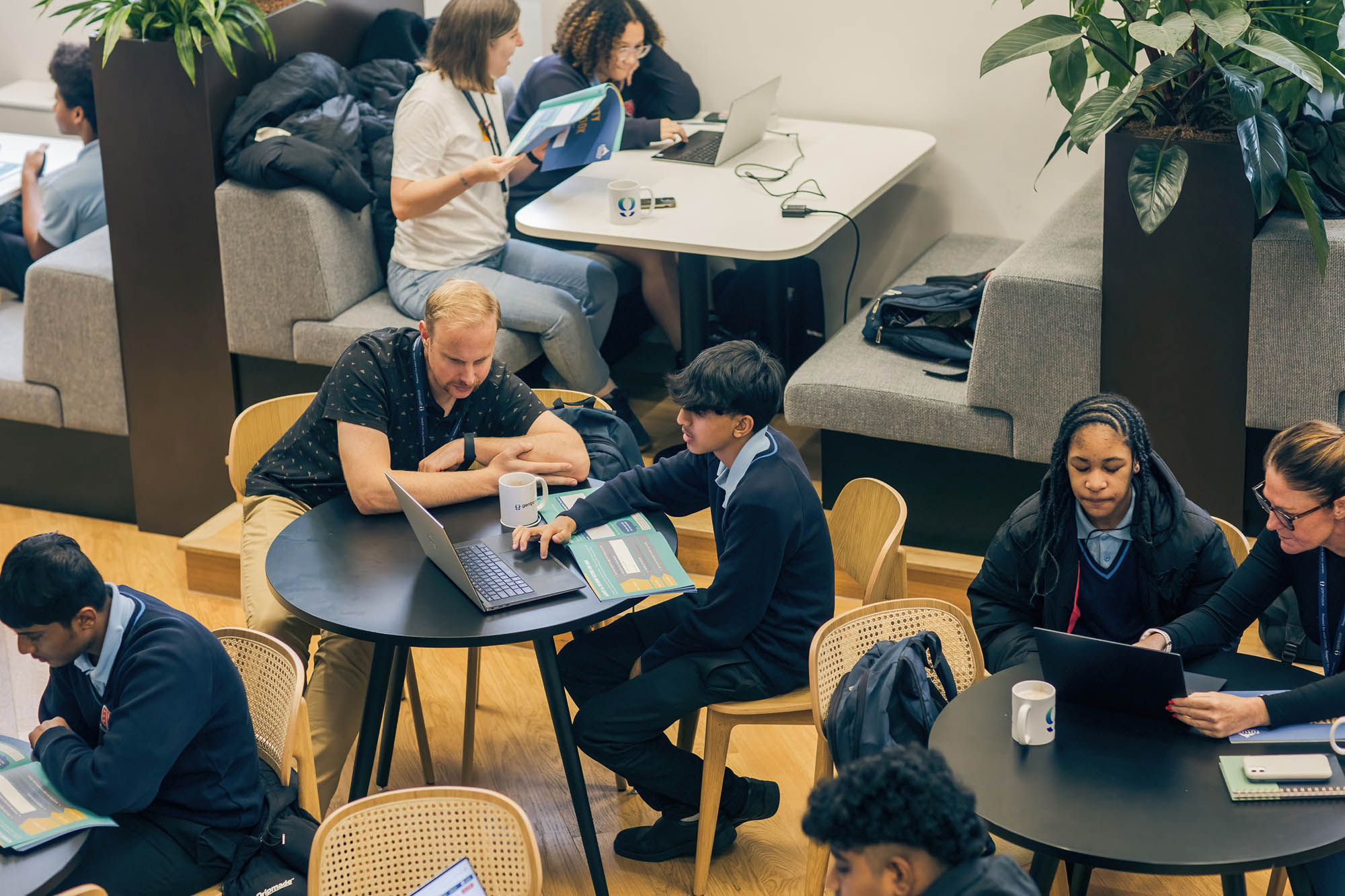 people seated at round tables in a room with laptops