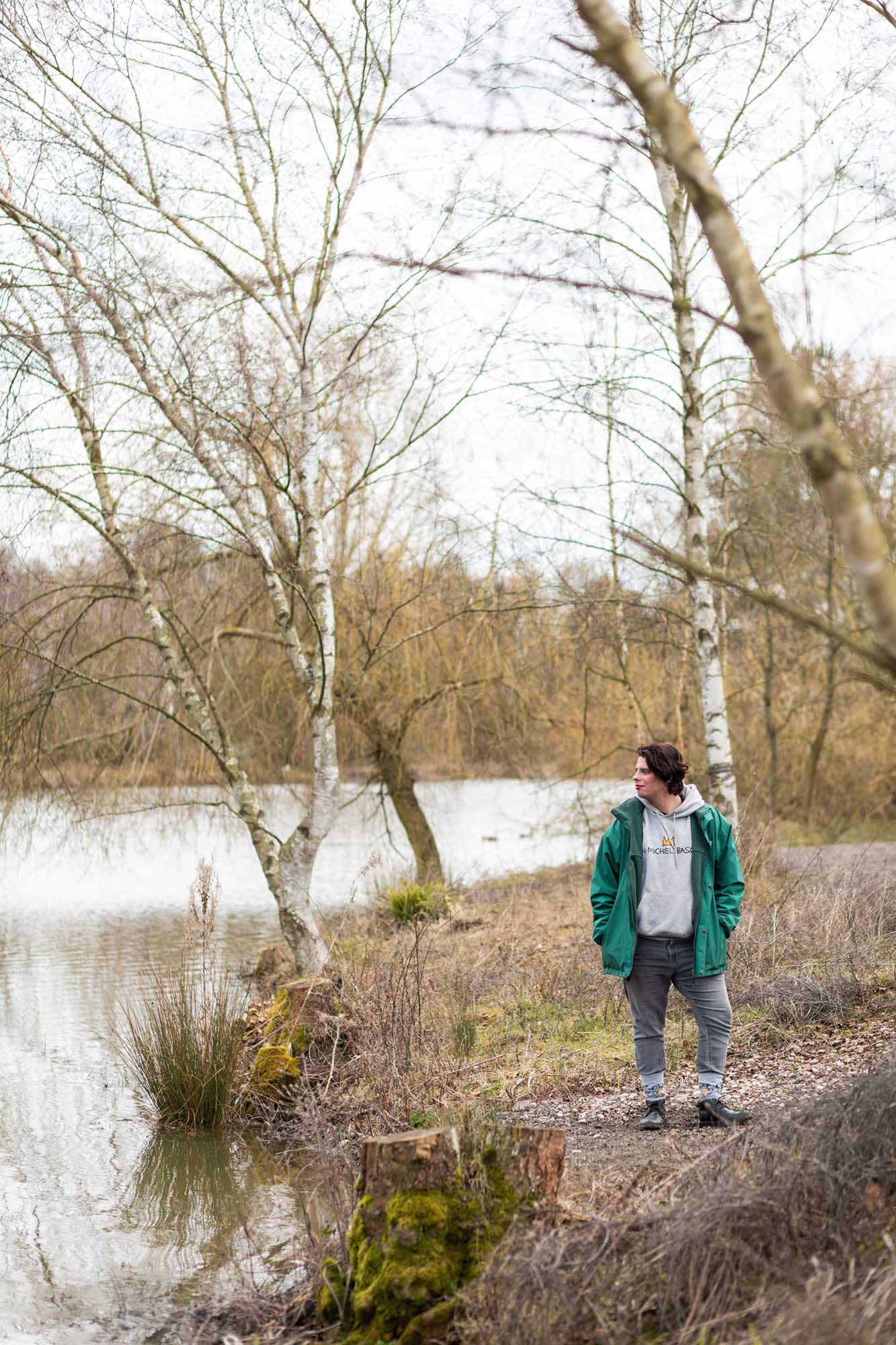 a person in a green jacket standing by a lake in the forest