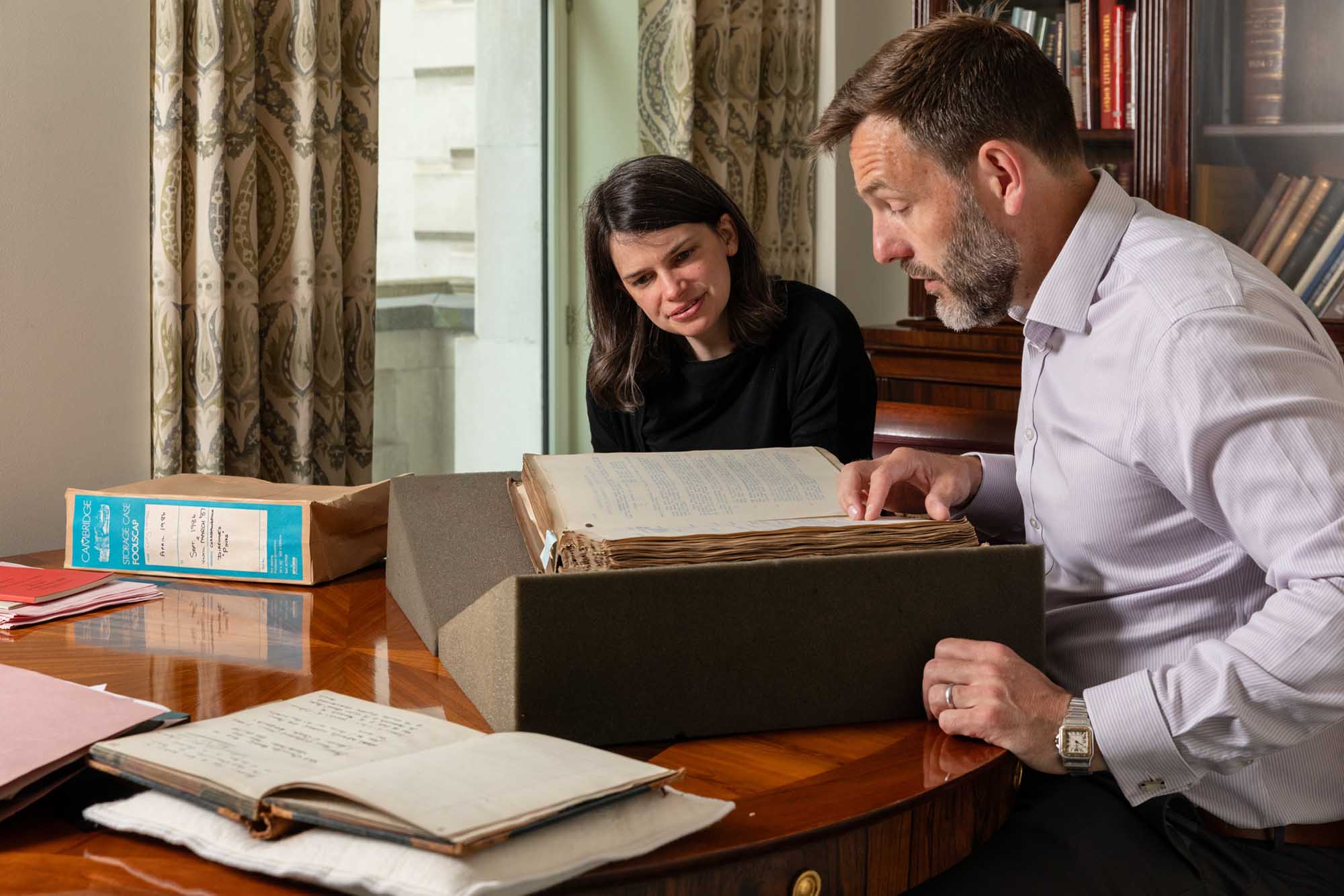 man and a woman sitting at table looking at an old book