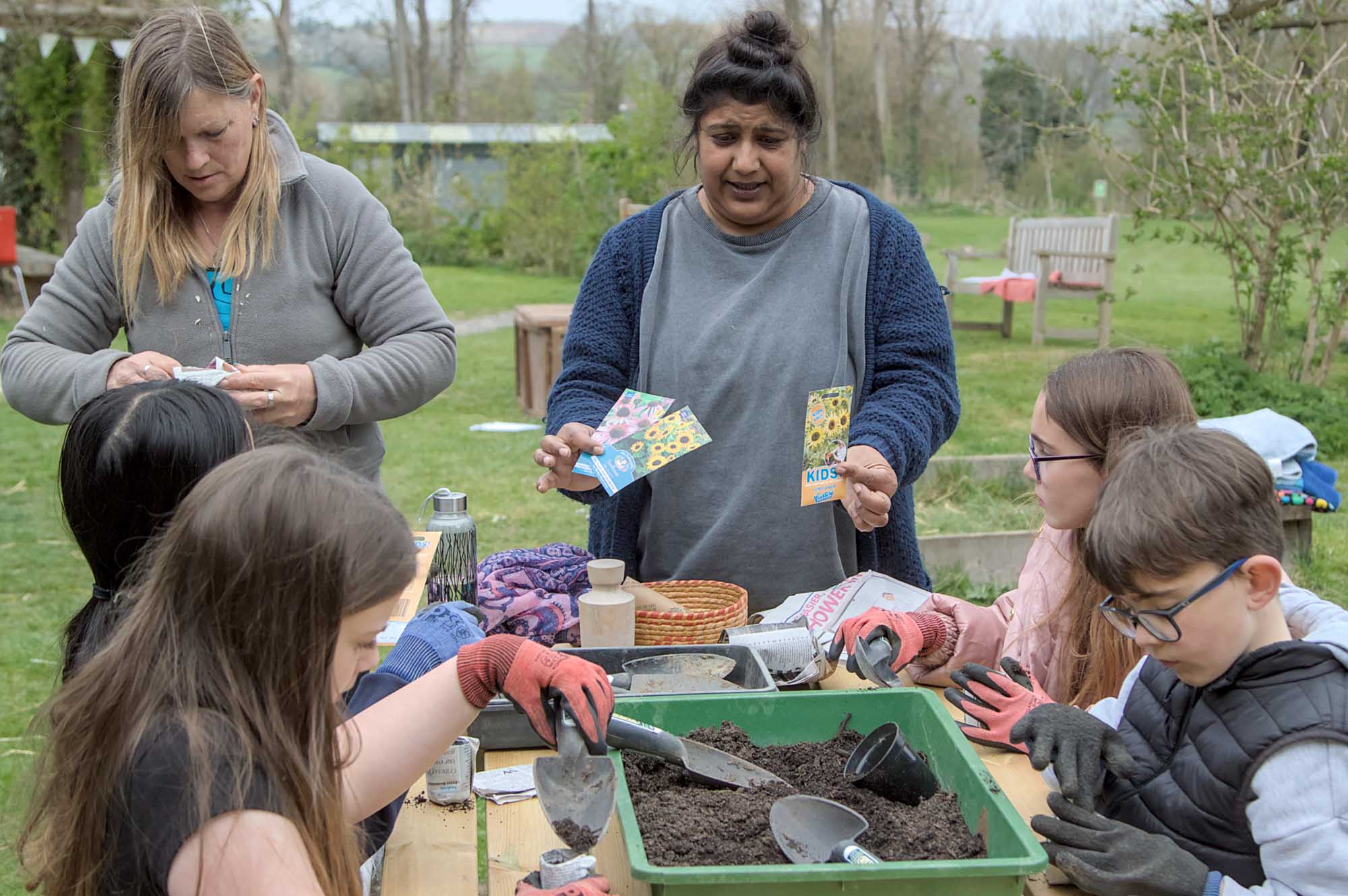 woman outside with children on a bench planting seeds
